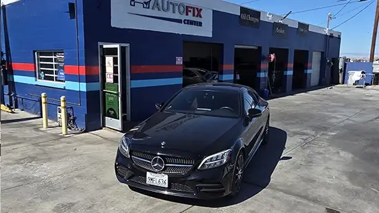 Black car parked in front of a blue auto repair building.